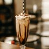 Vertical shot of a glass full of coffee milkshake with a striped straw in it